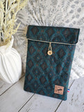 Pochette tissu bleu motif géométrique, bouton bois, sur fond végétal décoratif.