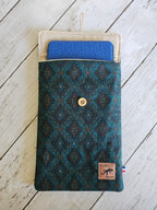 Pochette textile motif géométrique bleu-vert avec bouton, tablette bleue à l’intérieur, accessoire mode.
