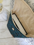 Pochette tissu bleu motif bohème avec bouton, contenant un livre, sur fond en bois clair.