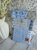 Pochette patchwork en tissu fleuri bleu et beige avec bouton en bois, posée sur table en bois clair