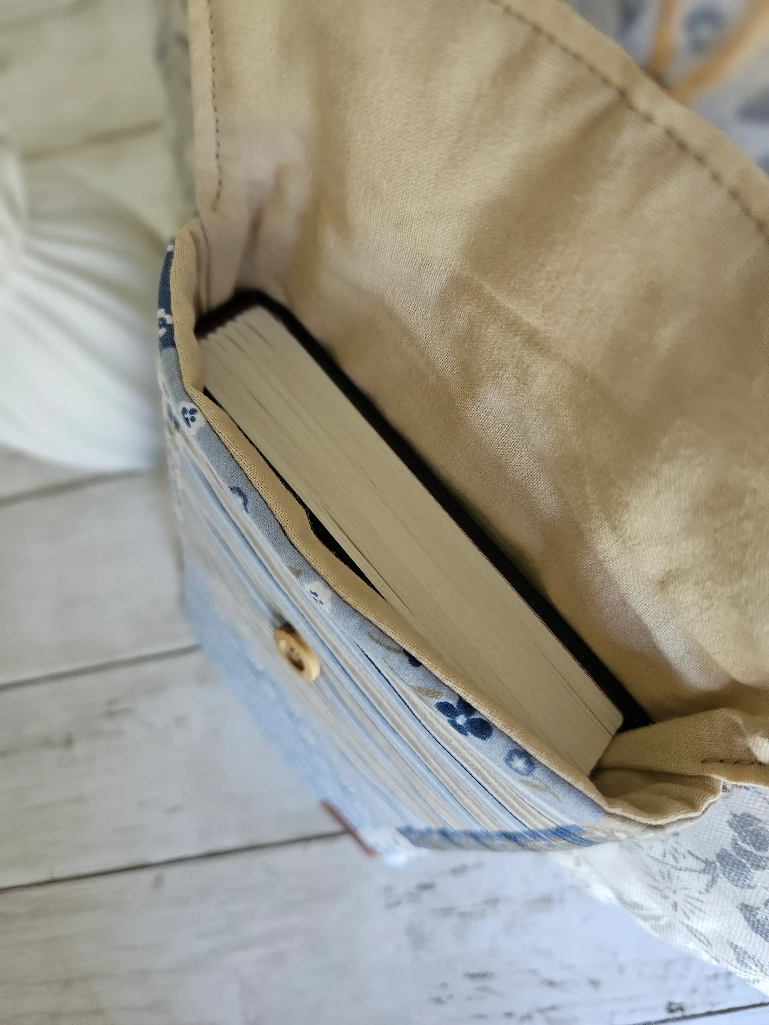 Intérieur d’un sac en tissu à motif fleuri bleu avec un livre à l’intérieur, posé sur bois blanc