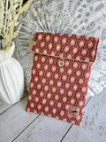 Pochette tissu motif rouge et rose avec bouton, posée sur table en bois, déco végétale