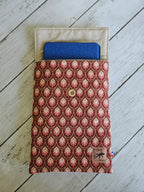 Pochette tissu motif rose avec bouton en bois, contenant une tablette bleue, sur fond bois.