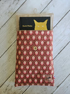 Pochette en tissu imprimé rouge rose avec bouton, contenant un livre, sur fond bois blanc.