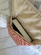 Petit sac à motif rouge et crème contenant un livre, posé sur une table en bois clair.