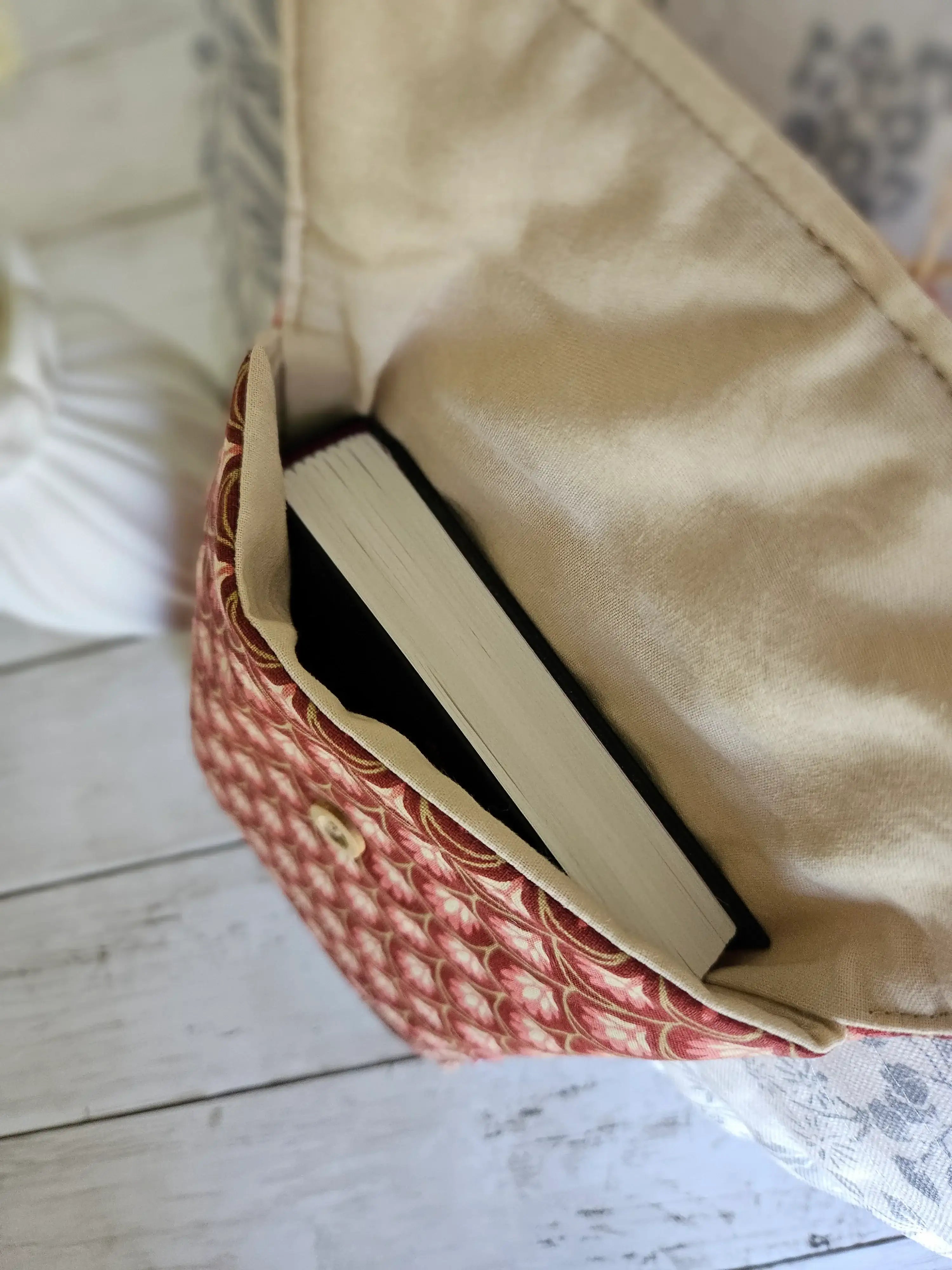 Petit sac à motif rouge et crème contenant un livre, posé sur une table en bois clair.