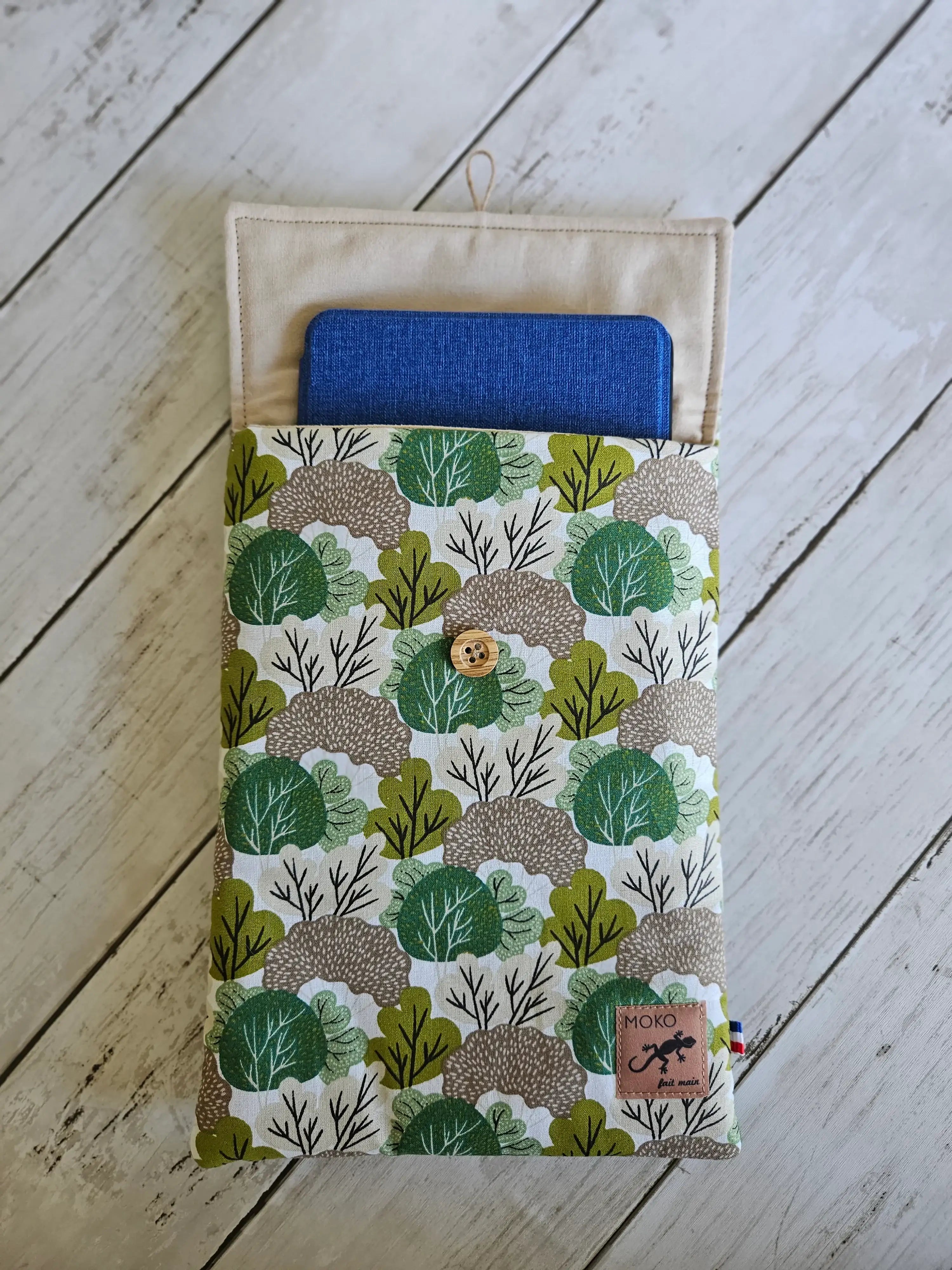 Pochette tablette motif feuillage vert et beige, bouton bois, sur fond bois clair.