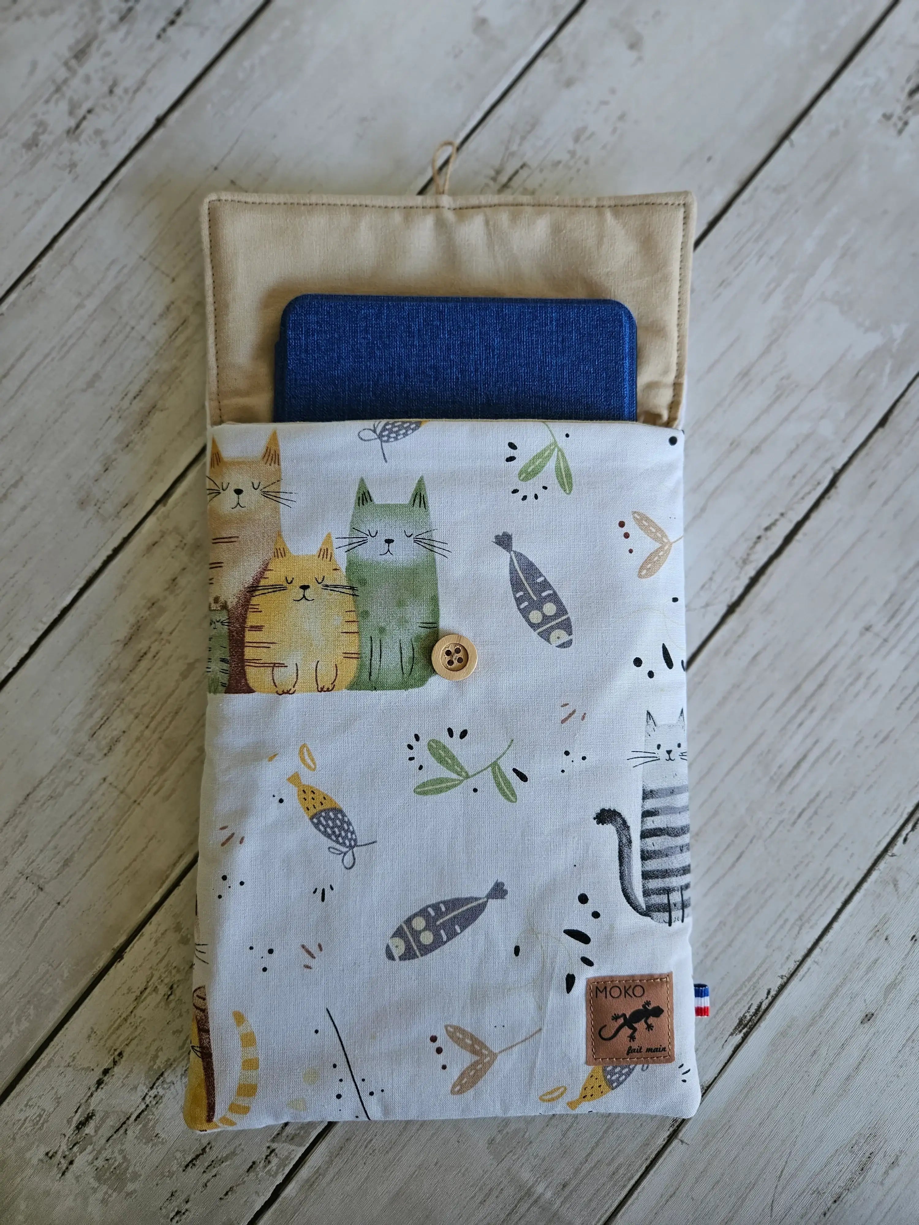 Pochette en tissu imprimé chats pour liseuse, fermée par bouton, posée sur fond bois clair