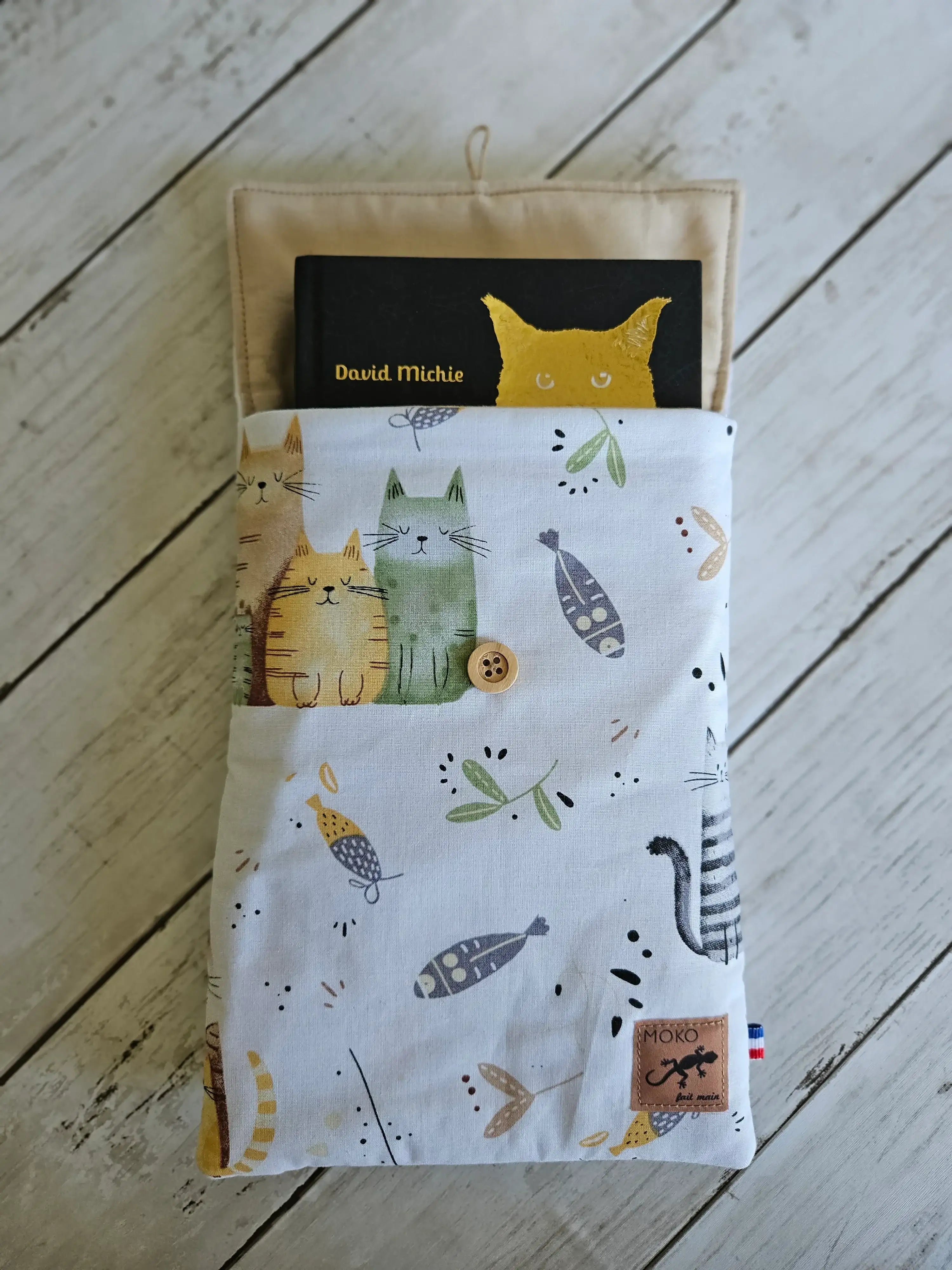 Pochette en tissu motif chats pour livre, accessoire de mode, sur fond bois clair.