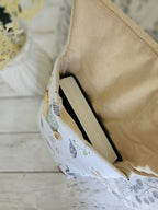 Petit sac en tissu à motif, doublure beige, contenant un livre, posé sur une surface blanche.