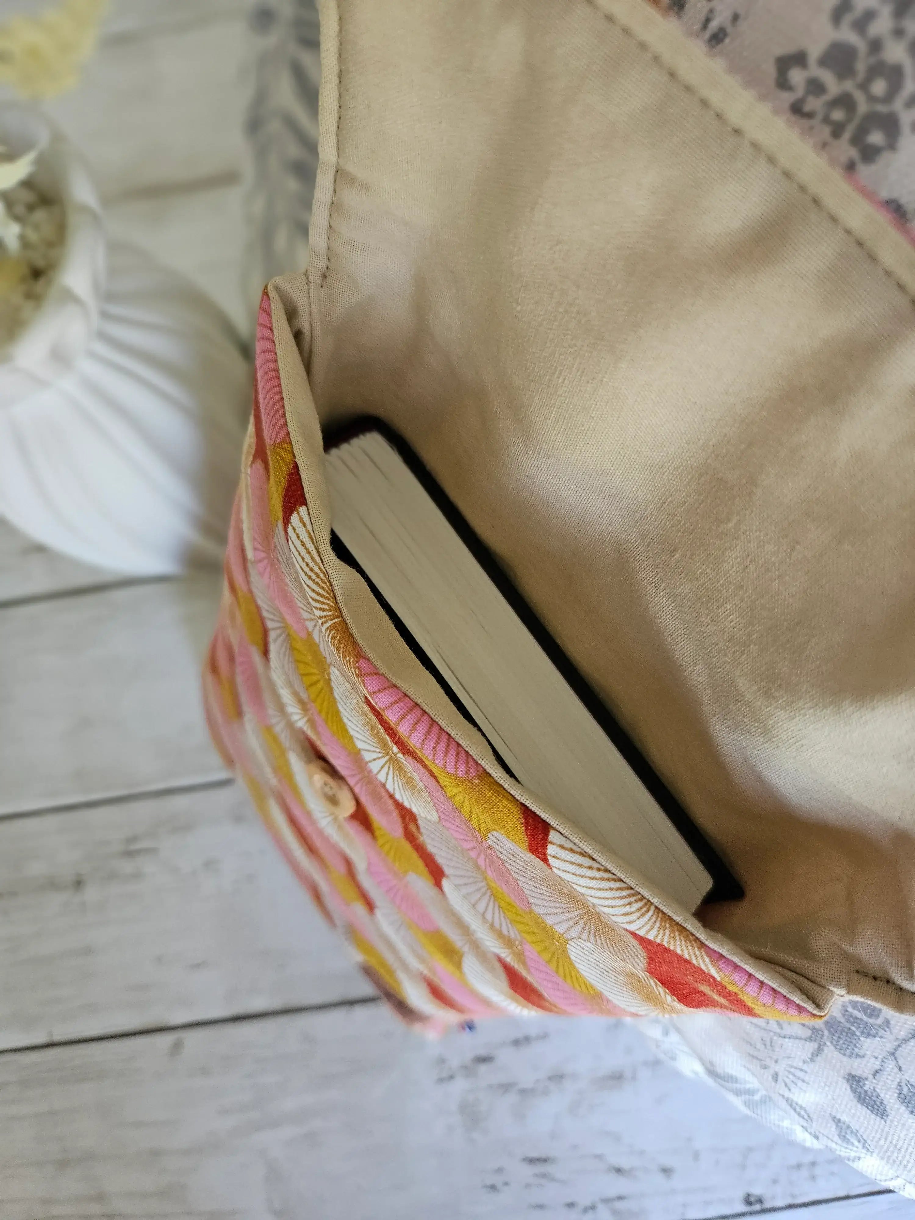 Housse à livre en tissu motifs colorés contenant un livre, posée sur une table en bois clair.