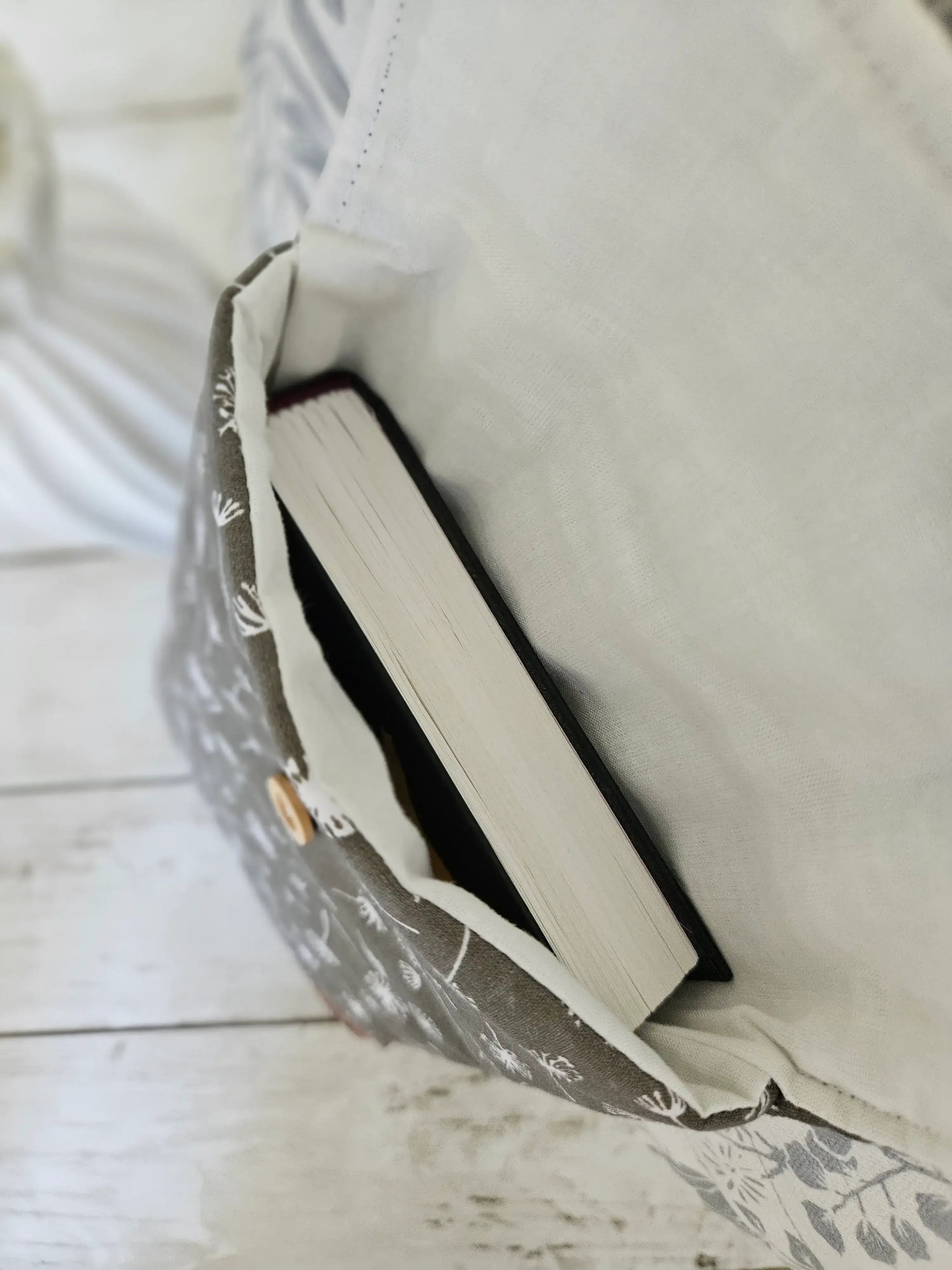 Housse à livre en tissu floral beige avec un livre à l'intérieur, bouton en bois visible.