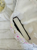 Housse à livre en tissu fleuri pastel avec livre à l'intérieur, sur fond bois blanc