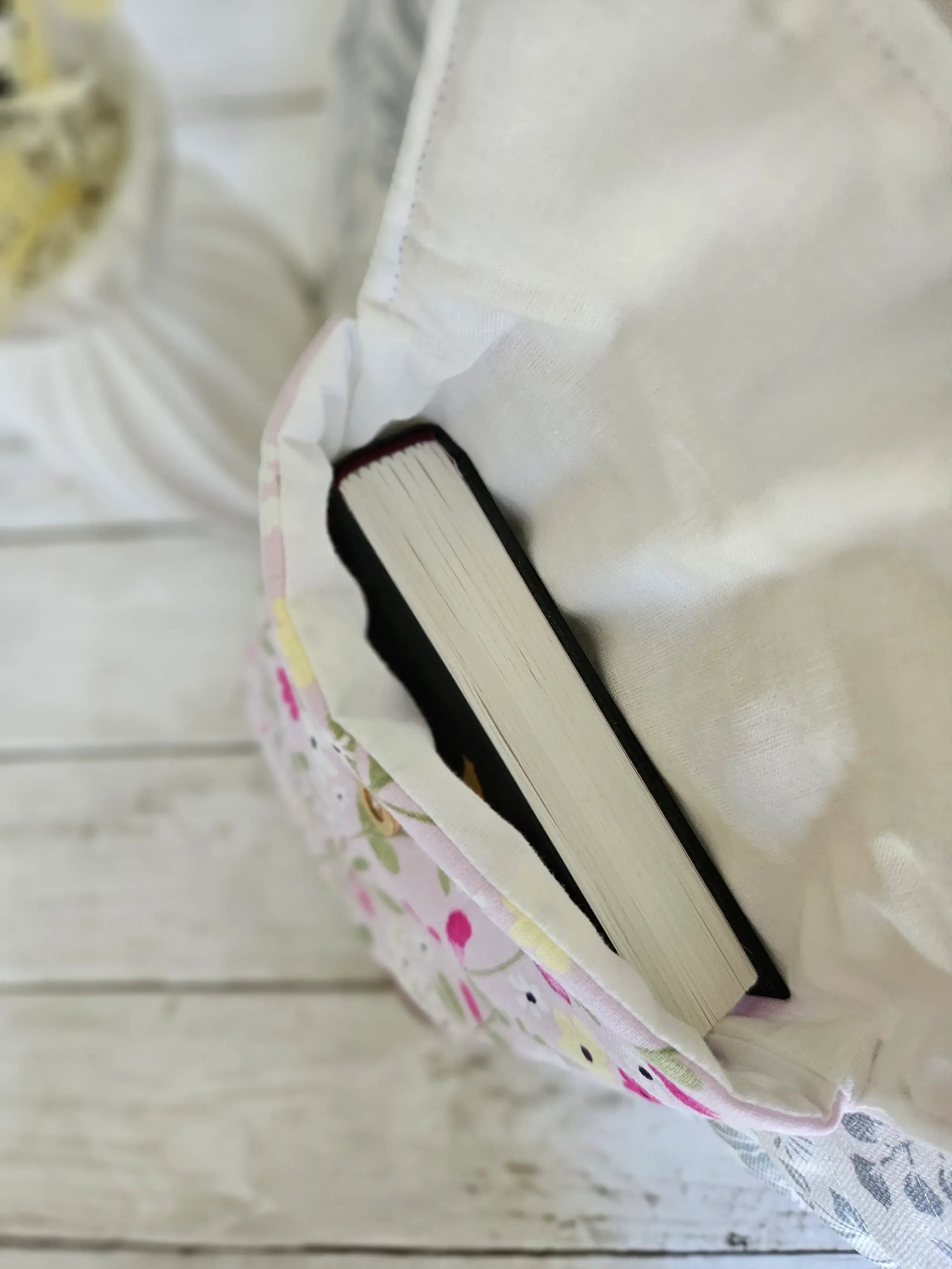 Housse à livre en tissu fleuri pastel avec livre à l'intérieur, sur fond bois blanc