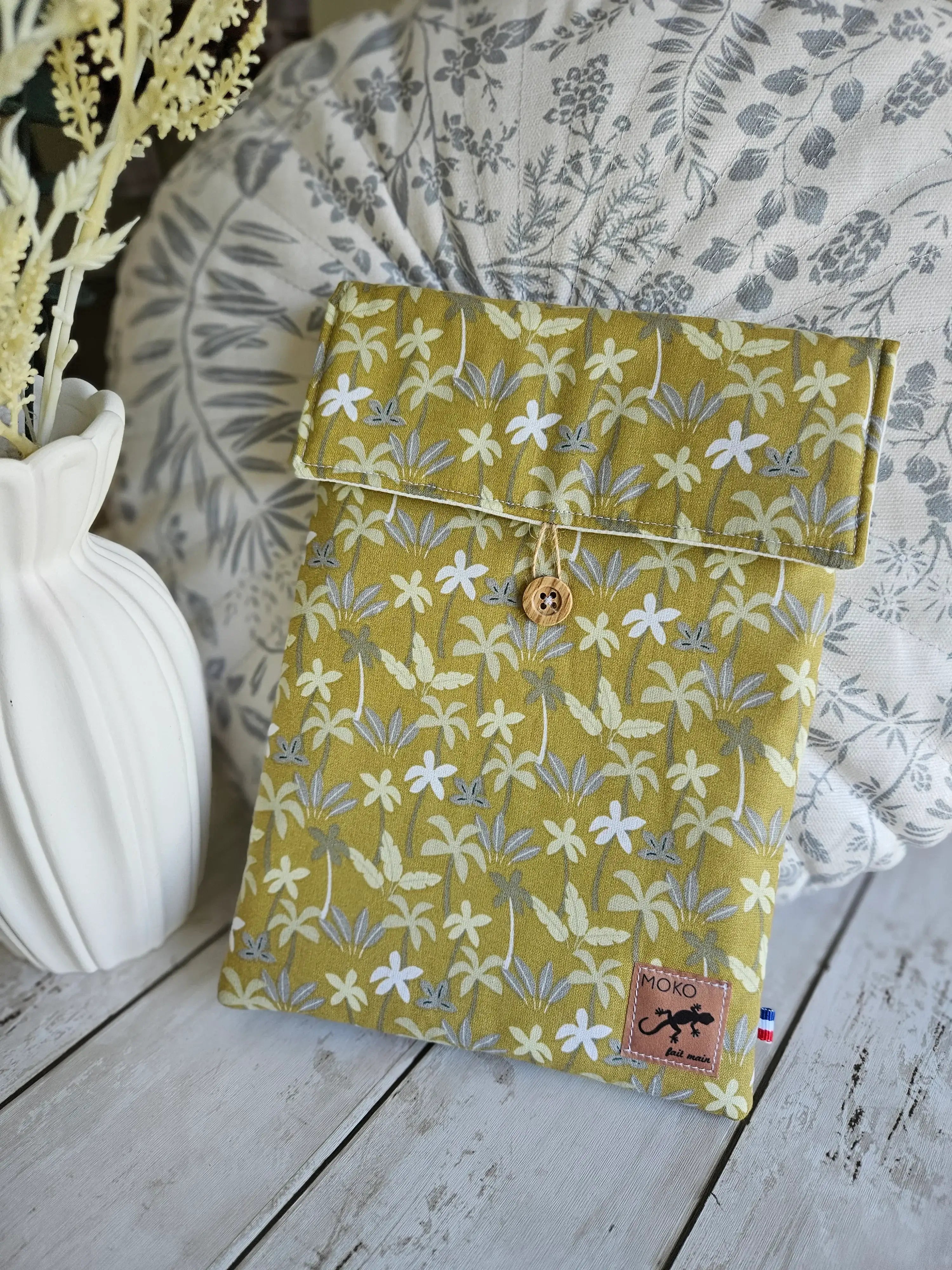 Housse à livre ou liseuse artisanale tissu jaune motif floral, bouton bois, posée sur table en bois.