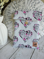 Housse à livre liseuse en tissu à motifs cœurs, fermée par un bouton, sur fond décoratif.