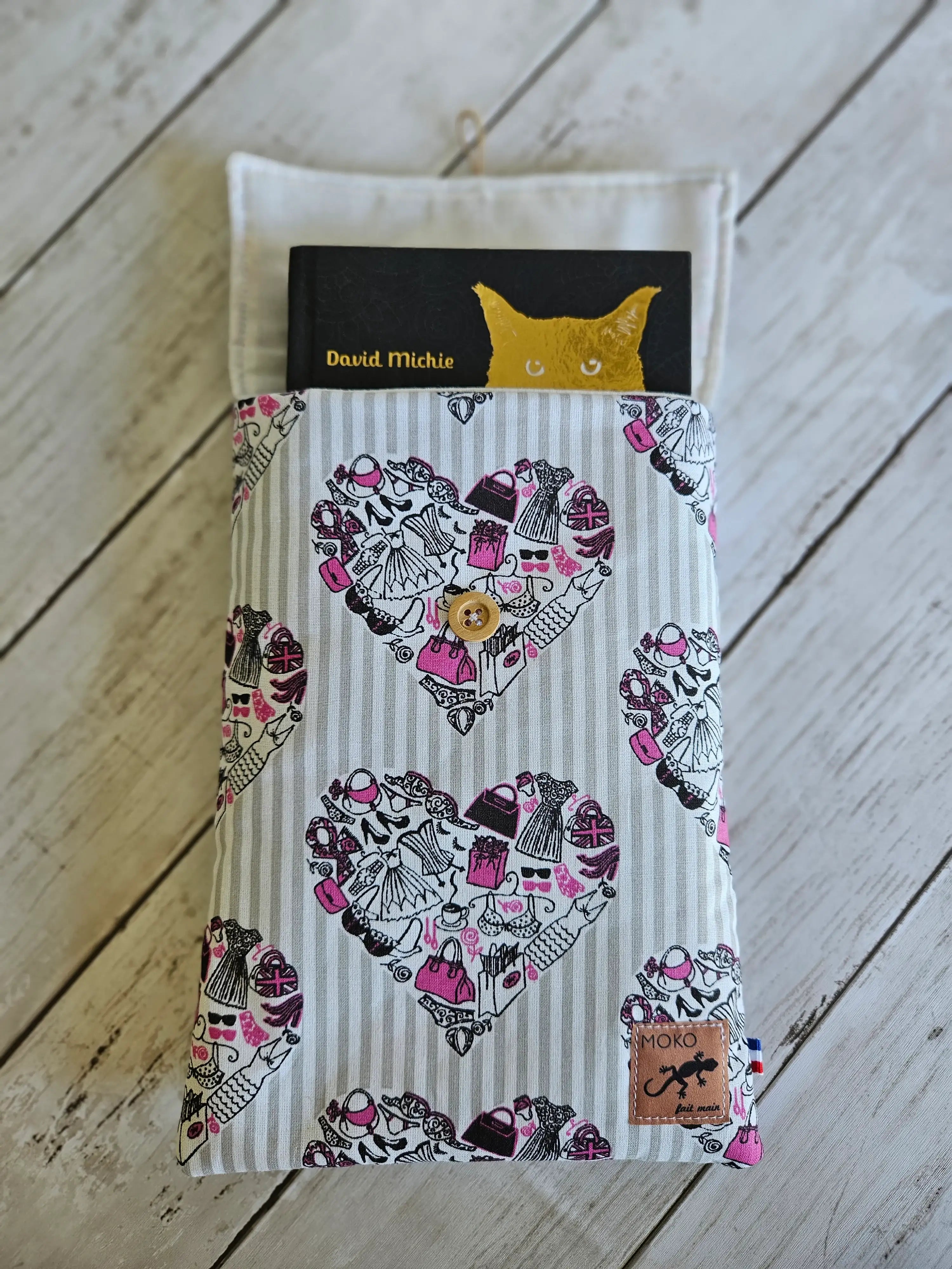 Housse à livre liseuse en tissu à motifs cœurs couture, bouton bois, sur fond bois clair.