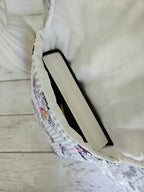 Housse à livre artisanale en tissu blanc et motifs, contenant un livre, vue de dessus