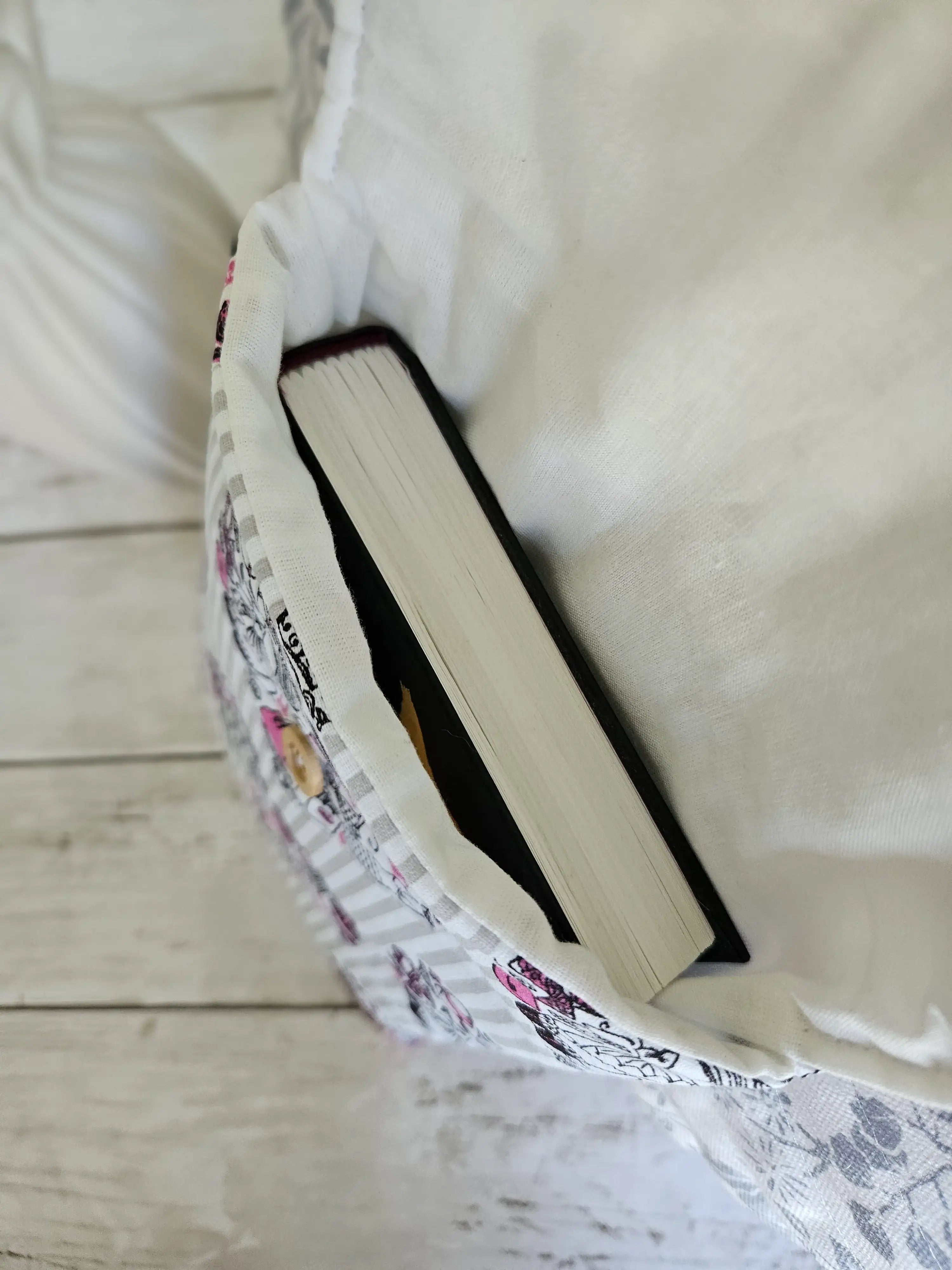 Housse à livre artisanale en tissu blanc et motifs, contenant un livre, vue de dessus