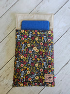 Housse à livre liseuse noire motifs squelettes et fleurs colorées sur fond en bois clair.