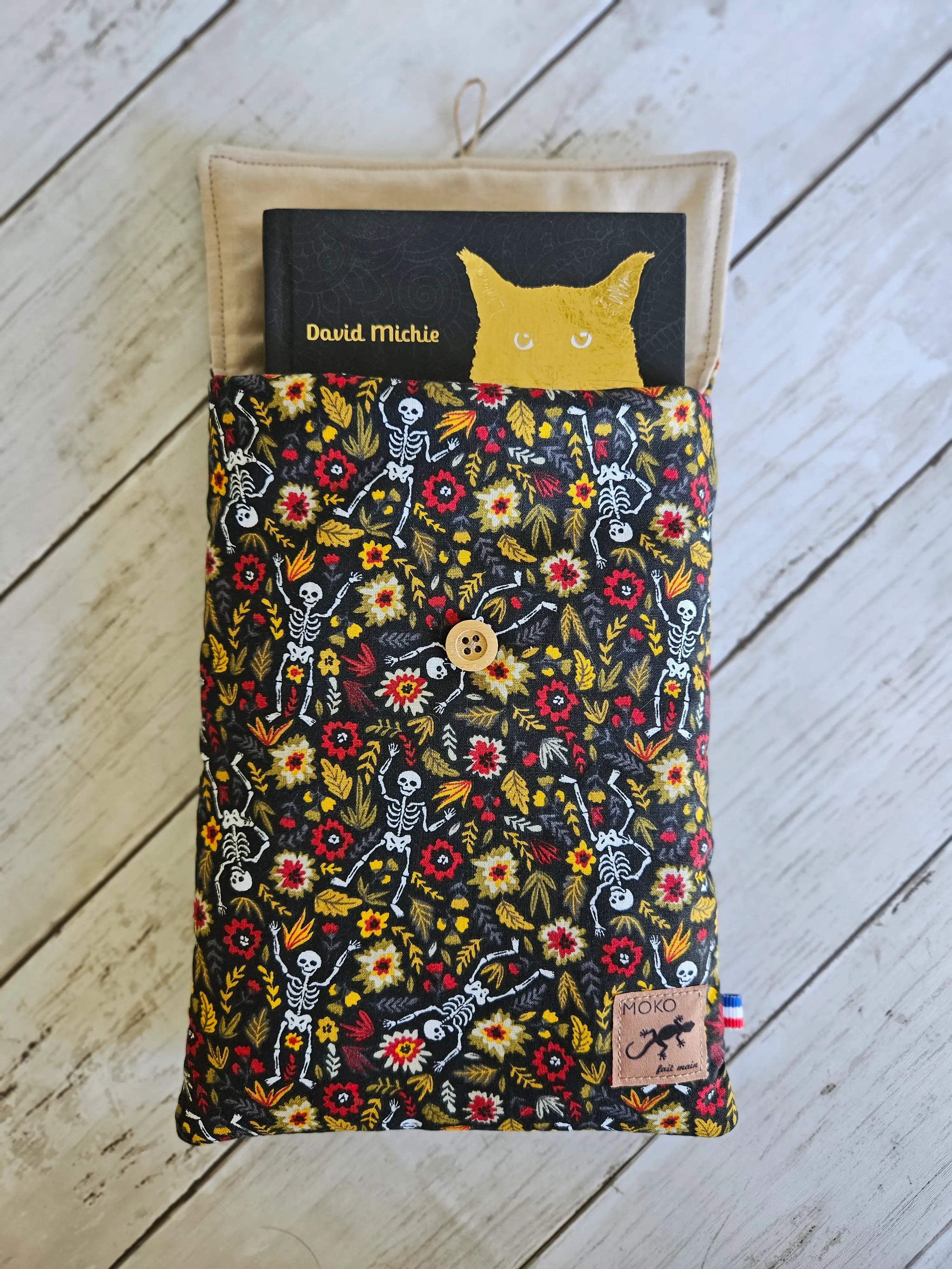 Housse à livre en tissu fleuri et motifs squelettes, bouton bois, sur fond en bois clair.