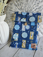 Housse à livre ou liseuse en tissu bleu motif plage, bouton en bois, pose sur fond clair.