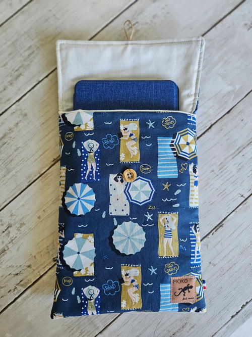 Étui tissu bleu à motifs plage, pour tablette, sur fond bois blanc.