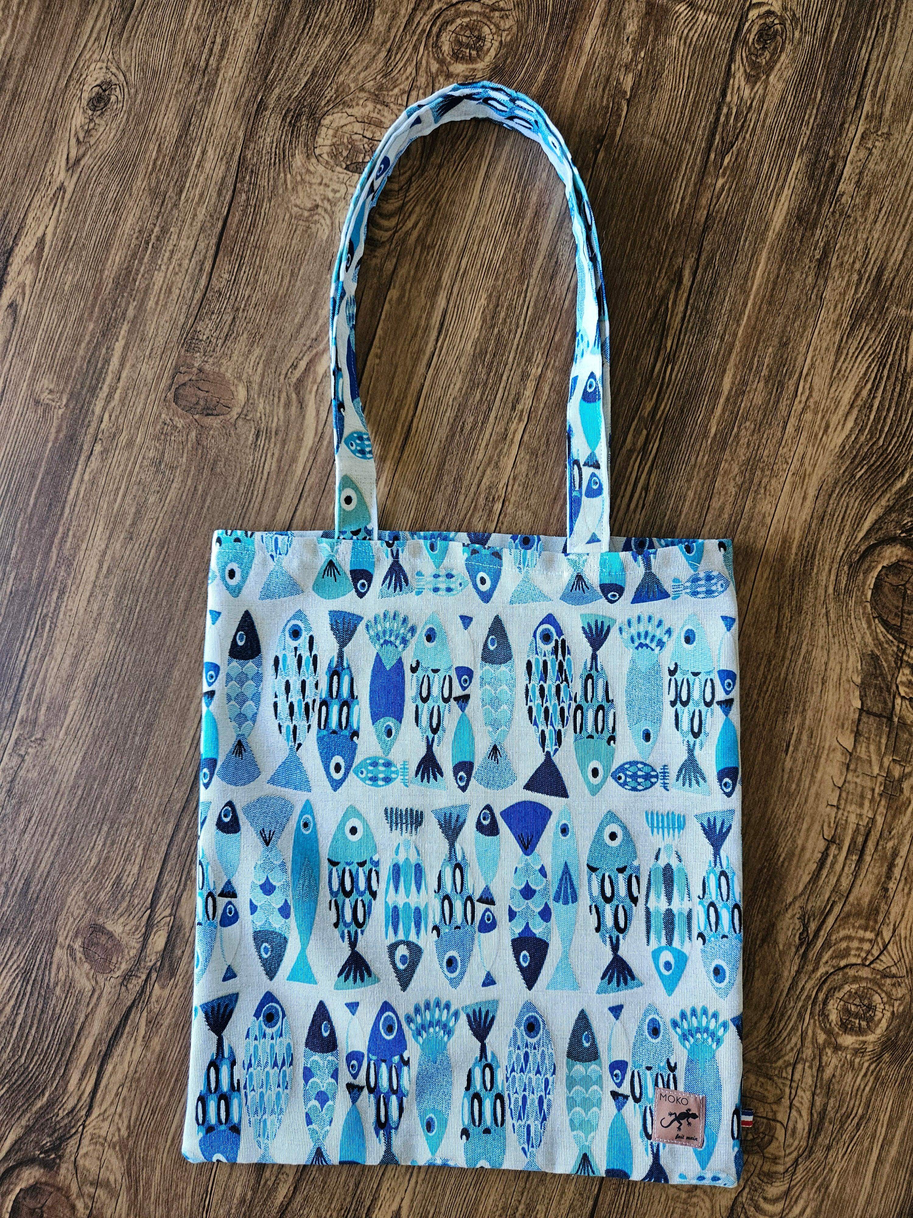 Sac cabas en tissu à motifs de poissons bleus, posé sur fond en bois, accessoire mode tendance.