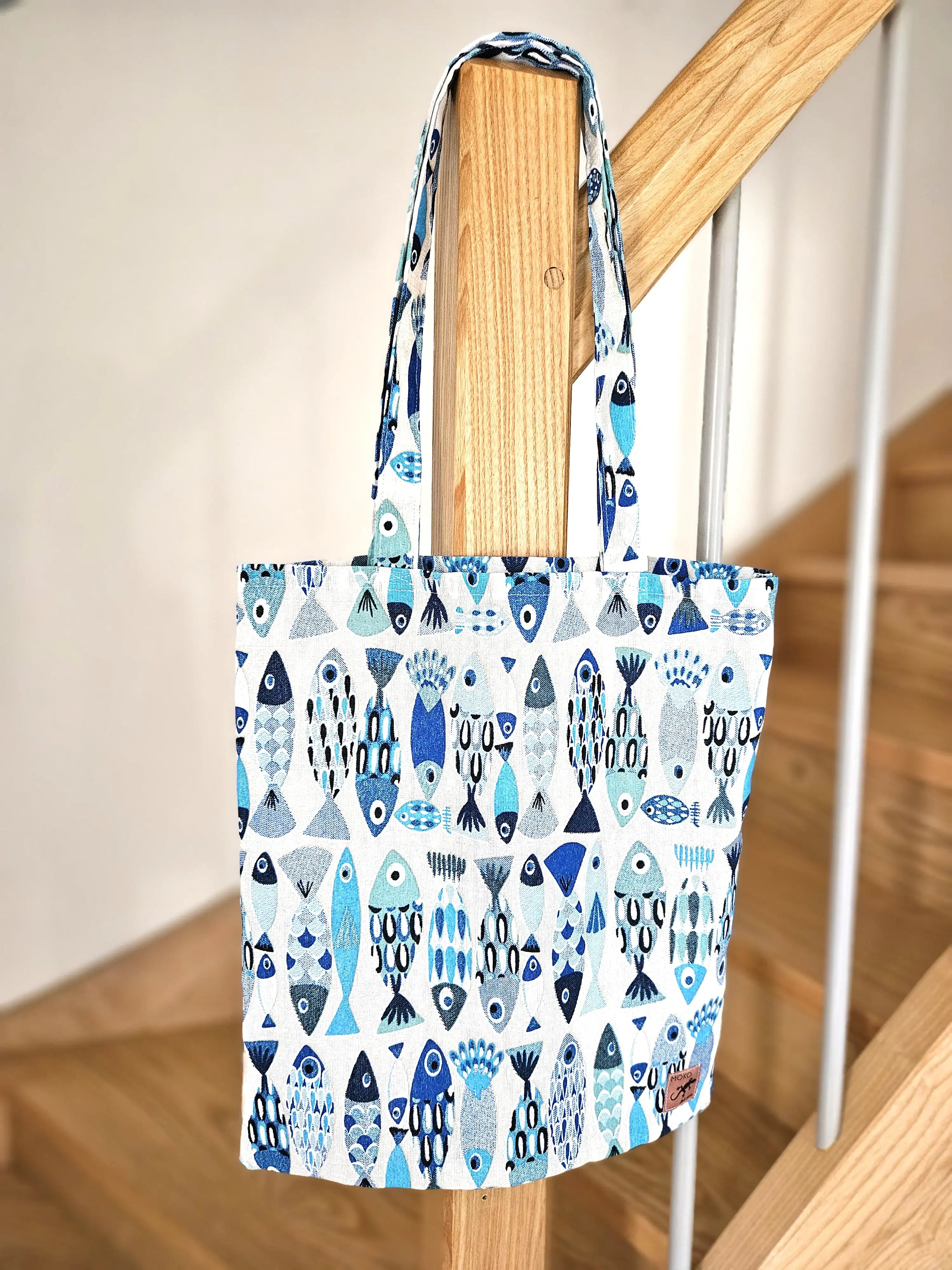 Totebag en tissu motif poissons bleus suspendu à une rambarde en bois, accessoire fait main.