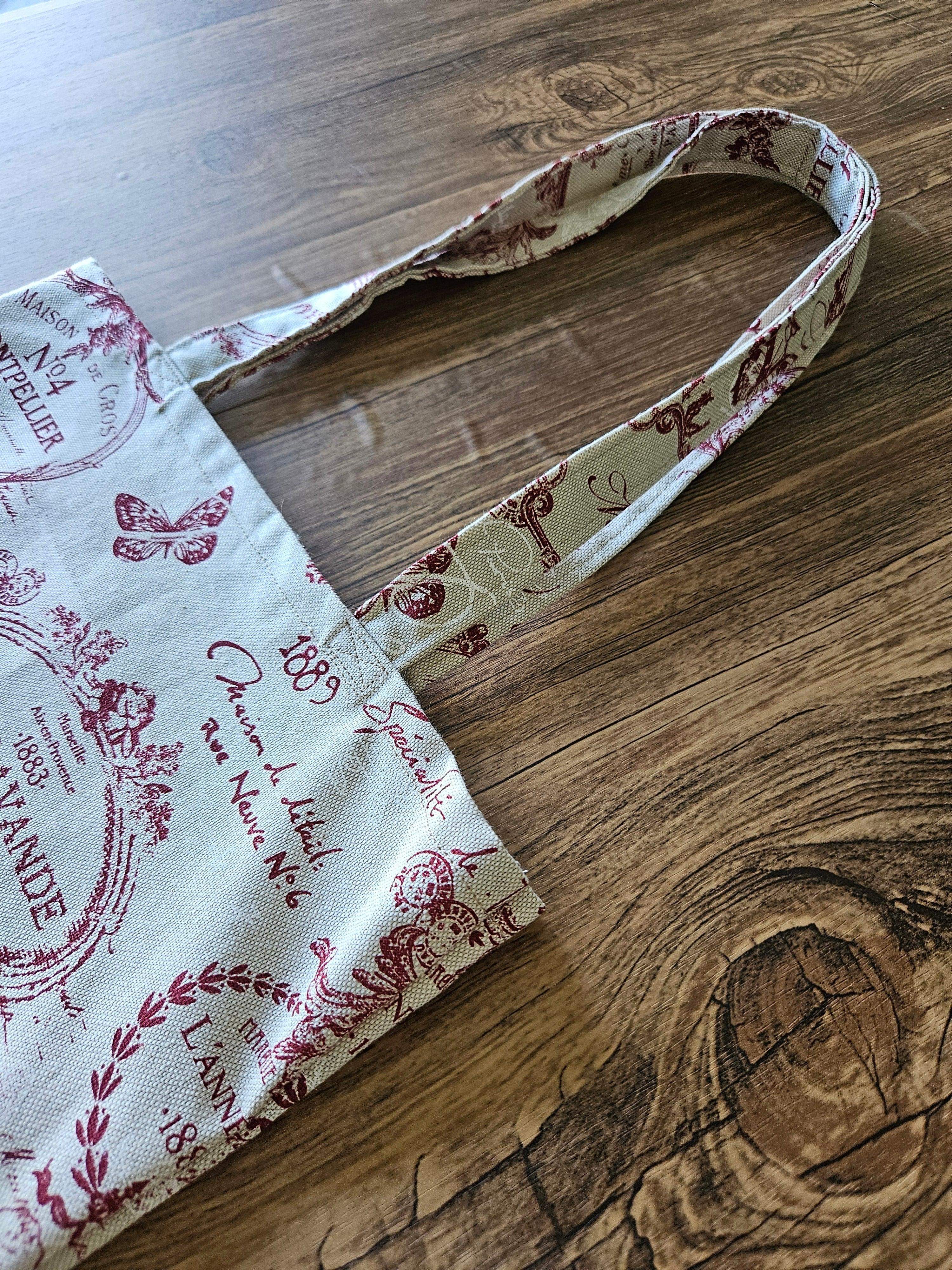 Sac en tissu imprimé écru et bordeaux avec anses, posé sur fond en bois, accessoire mode.