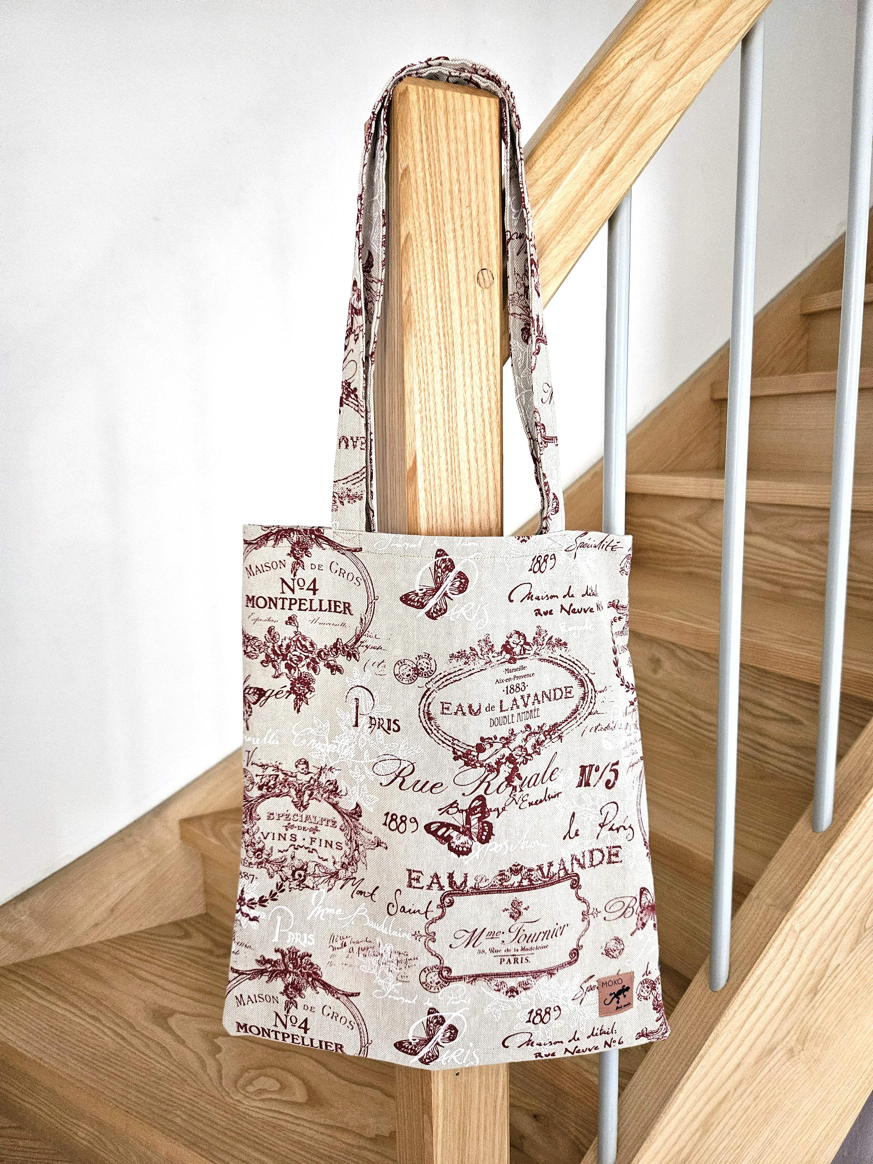 Totebag en tissu imprimé vintage lettres et papillons, posé sur une rambarde d'escalier en bois.