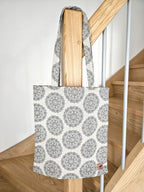 Totebag cabas motif mandala noir et blanc en tissu, suspendu sur une rampe d'escalier en bois