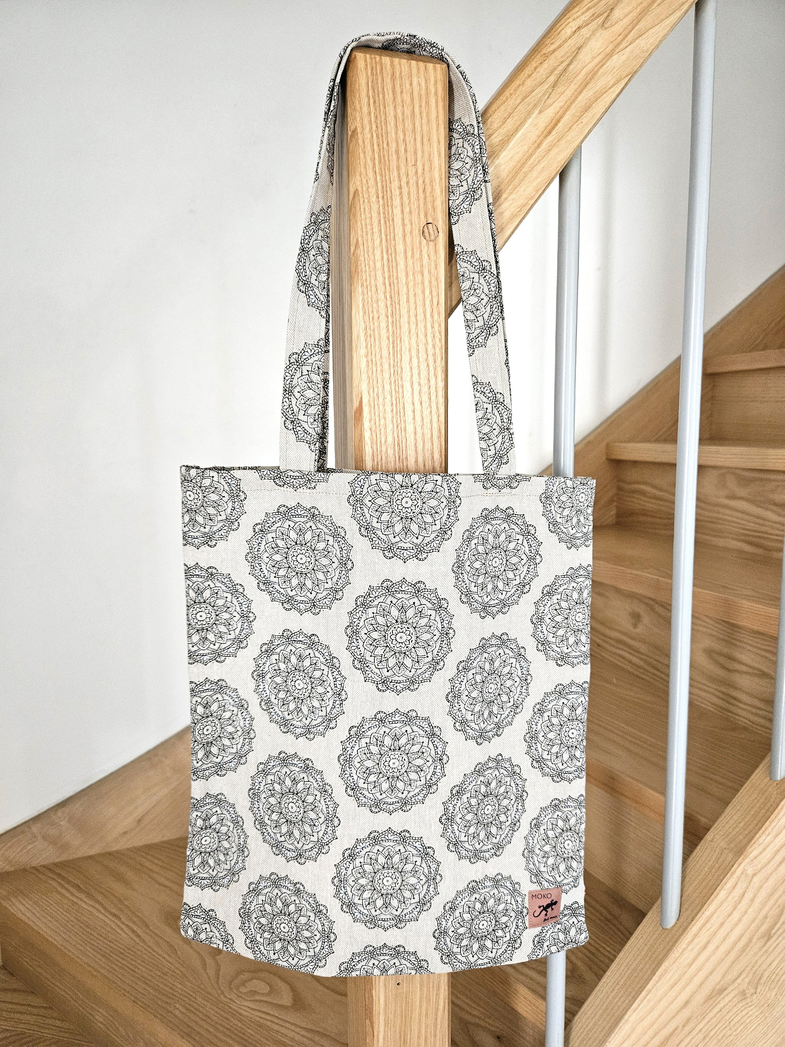 Totebag cabas motif mandala noir et blanc en tissu, suspendu sur une rampe d'escalier en bois
