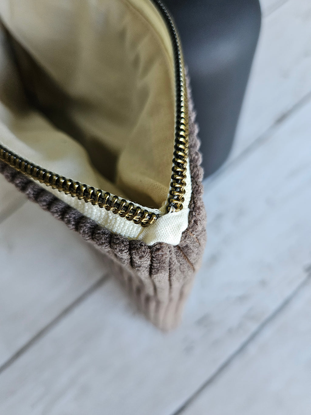 Trousse en velours marron à zip doré, vue de dessus sur fond bois clair