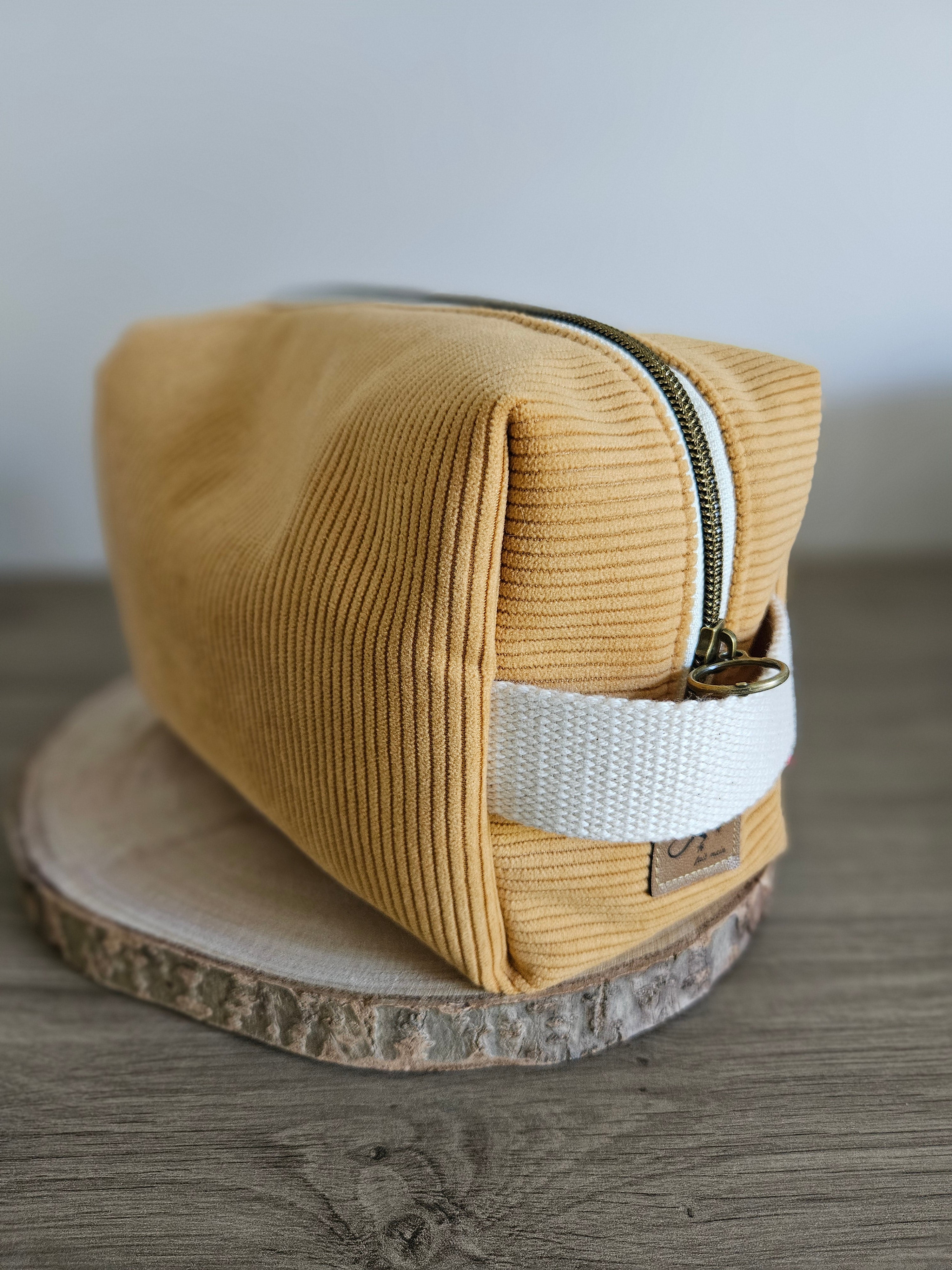 Trousse de toilette jaune moutarde en tissu côtelé avec poignée blanche, posée sur bois