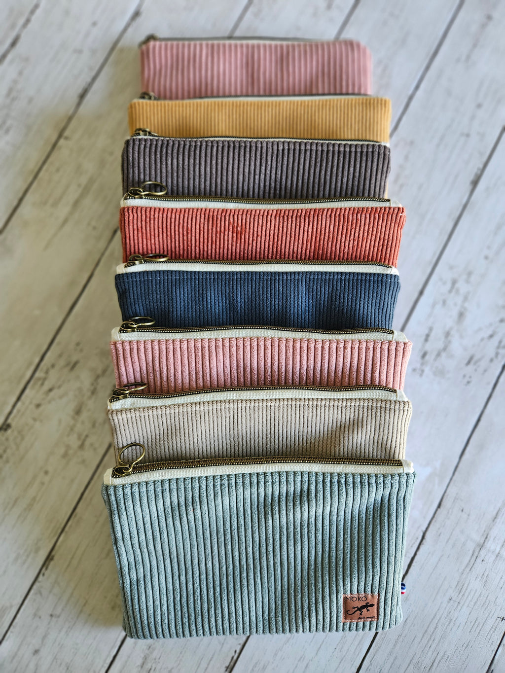 Trousse plate en velours côtelé beige, fermeture éclair, posée sur fond bois clair.