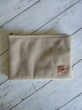 Trousse plate en velours beige côtelé avec zip, étiquette cuir, posée sur bois clair