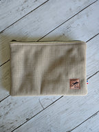 Trousse plate en velours beige côtelé avec zip, étiquette cuir, posée sur bois clair