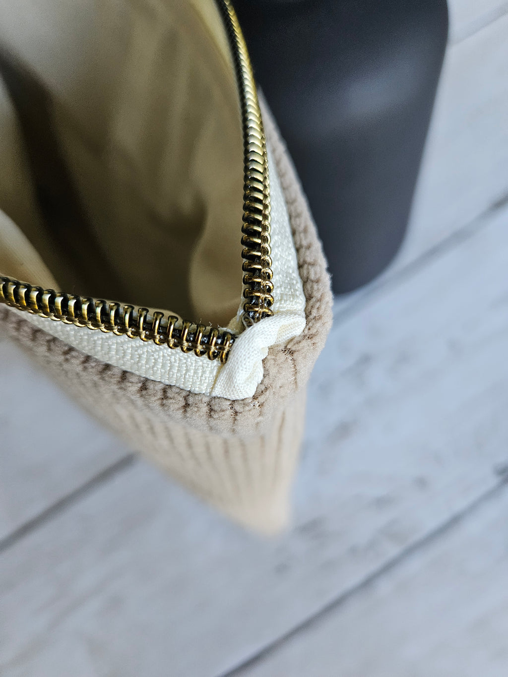 Trousse plate en velours beige avec fermeture éclair dorée, posée sur un fond en bois clair