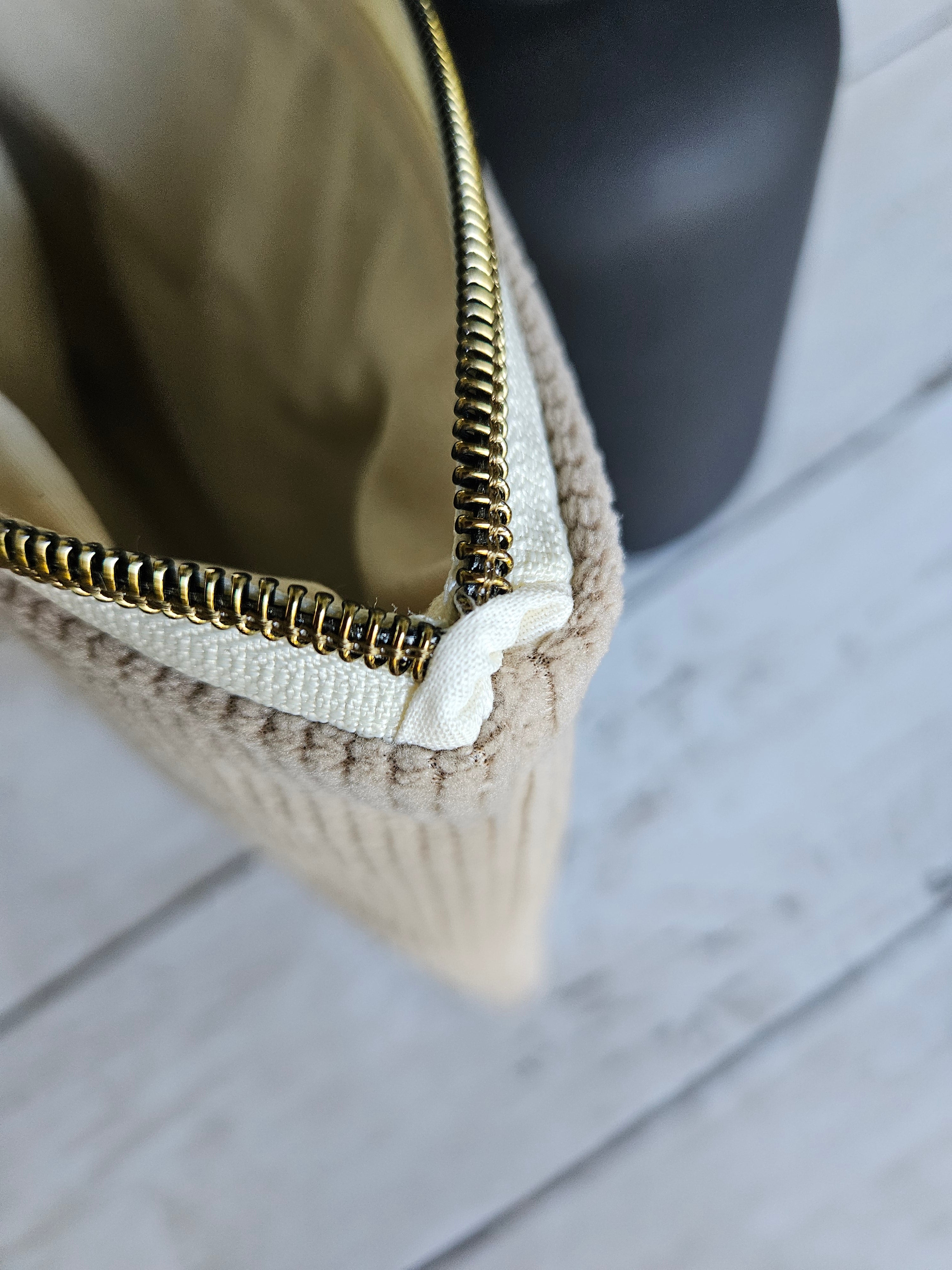Trousse plate en velours beige avec fermeture éclair dorée, posée sur un fond en bois clair