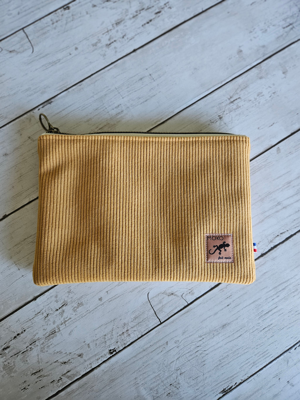 Trousse plate en velours jaune moutarde avec fermeture éclair, posée sur fond bois clair