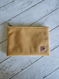 Trousse plate en velours jaune moutarde avec fermeture éclair, posée sur fond bois clair