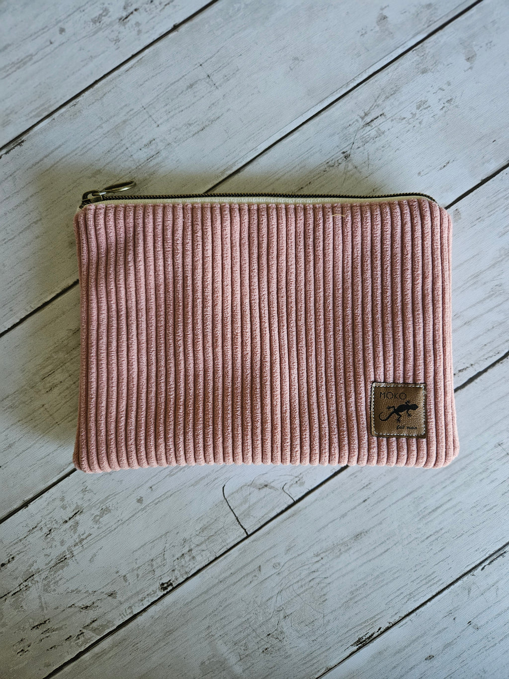Trousse plate en velours rose avec fermeture éclair, posée sur fond bois blanc.