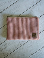 Trousse plate en velours rose avec fermeture éclair, posée sur fond bois blanc.