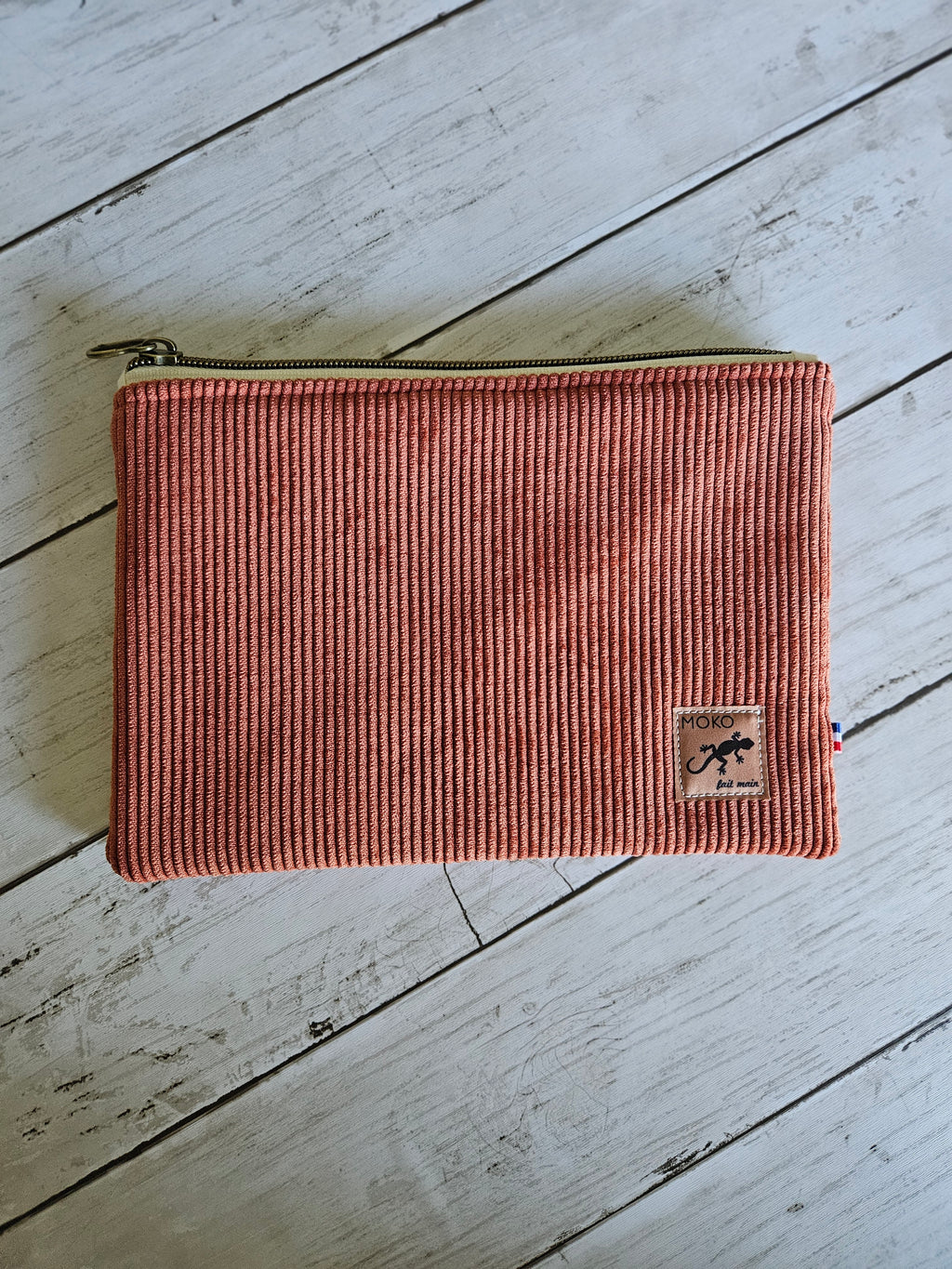 Trousse plate en velours côtelé terracotta avec fermeture éclair, posée sur fond bois.