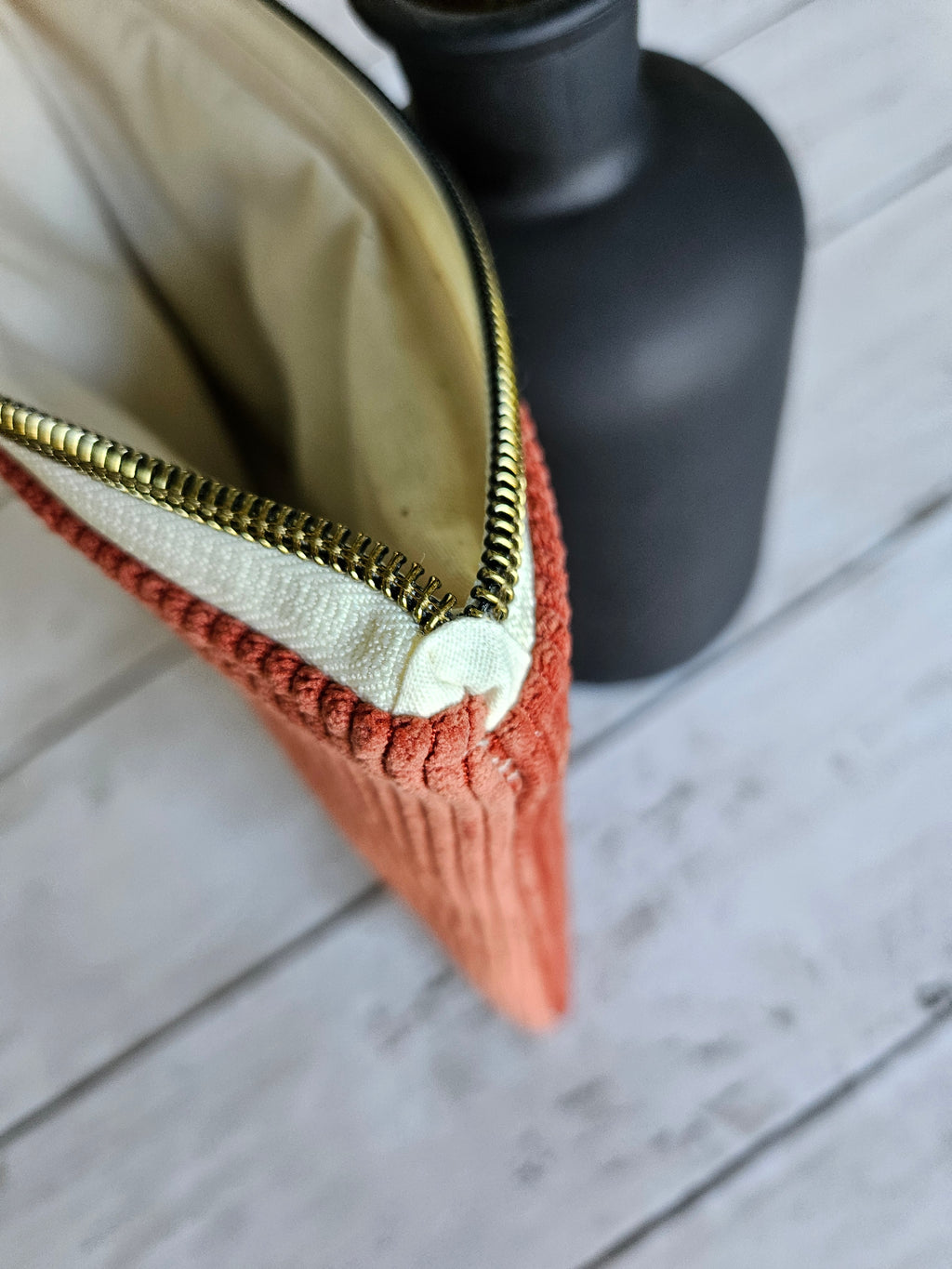 Trousse plate en velours terracotta zippée, posée sur fond bois clair, vue rapprochée