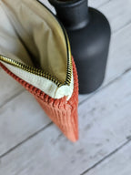 Trousse plate en velours terracotta zippée, posée sur fond bois clair, vue rapprochée
