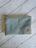 Trousse plate en velours vert d’eau avec fermeture éclair et étiquette cousue sur fond bois.