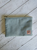 Trousse plate en velours vert d’eau avec fermeture éclair et étiquette cousue sur fond bois.