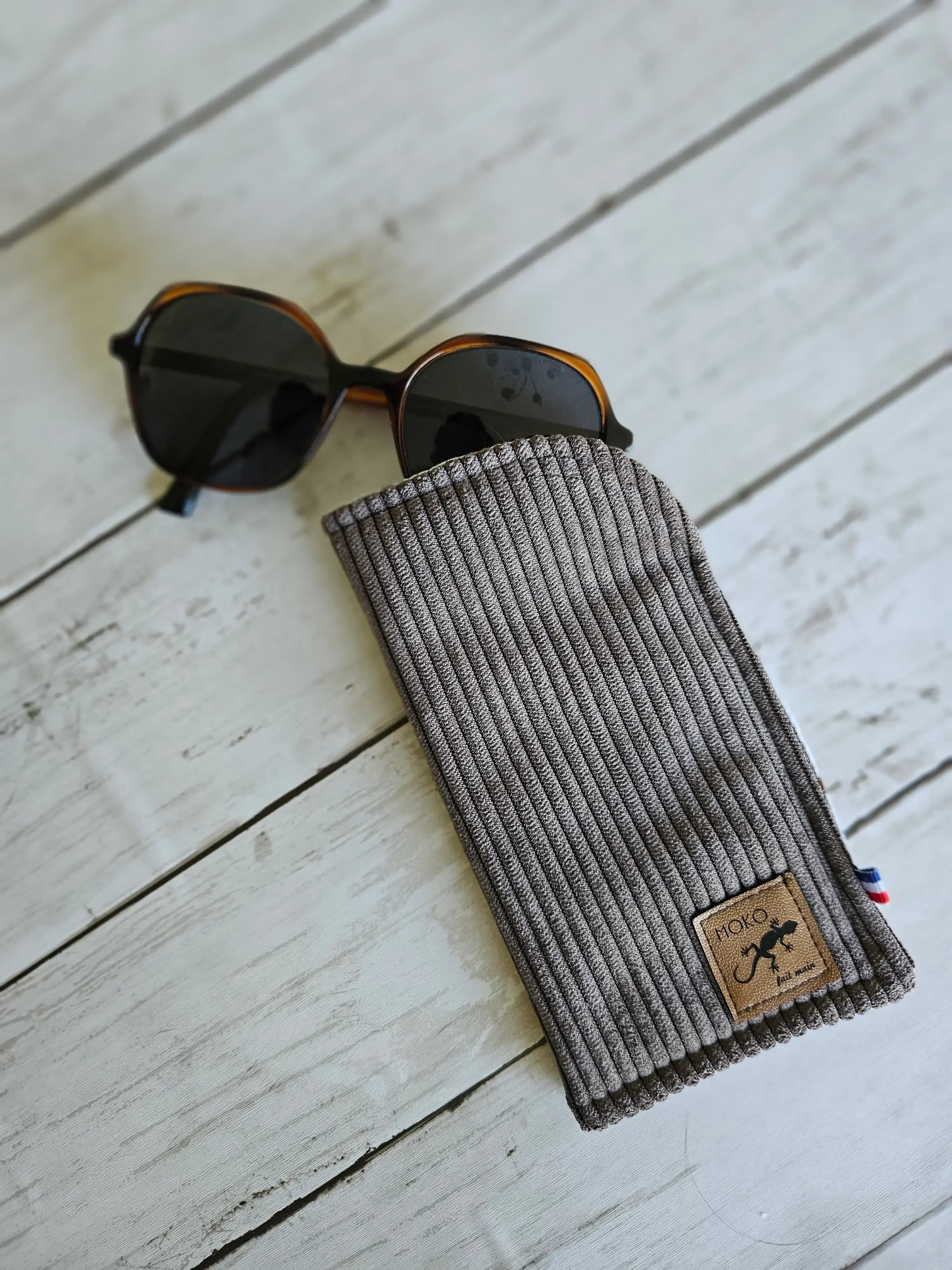 Étui à lunettes en velours côtelé gris avec lunettes de soleil sur fond bois clair